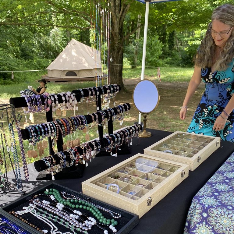 A vendor arranging handmade bracelets and necklaces on her table at an outdoor market